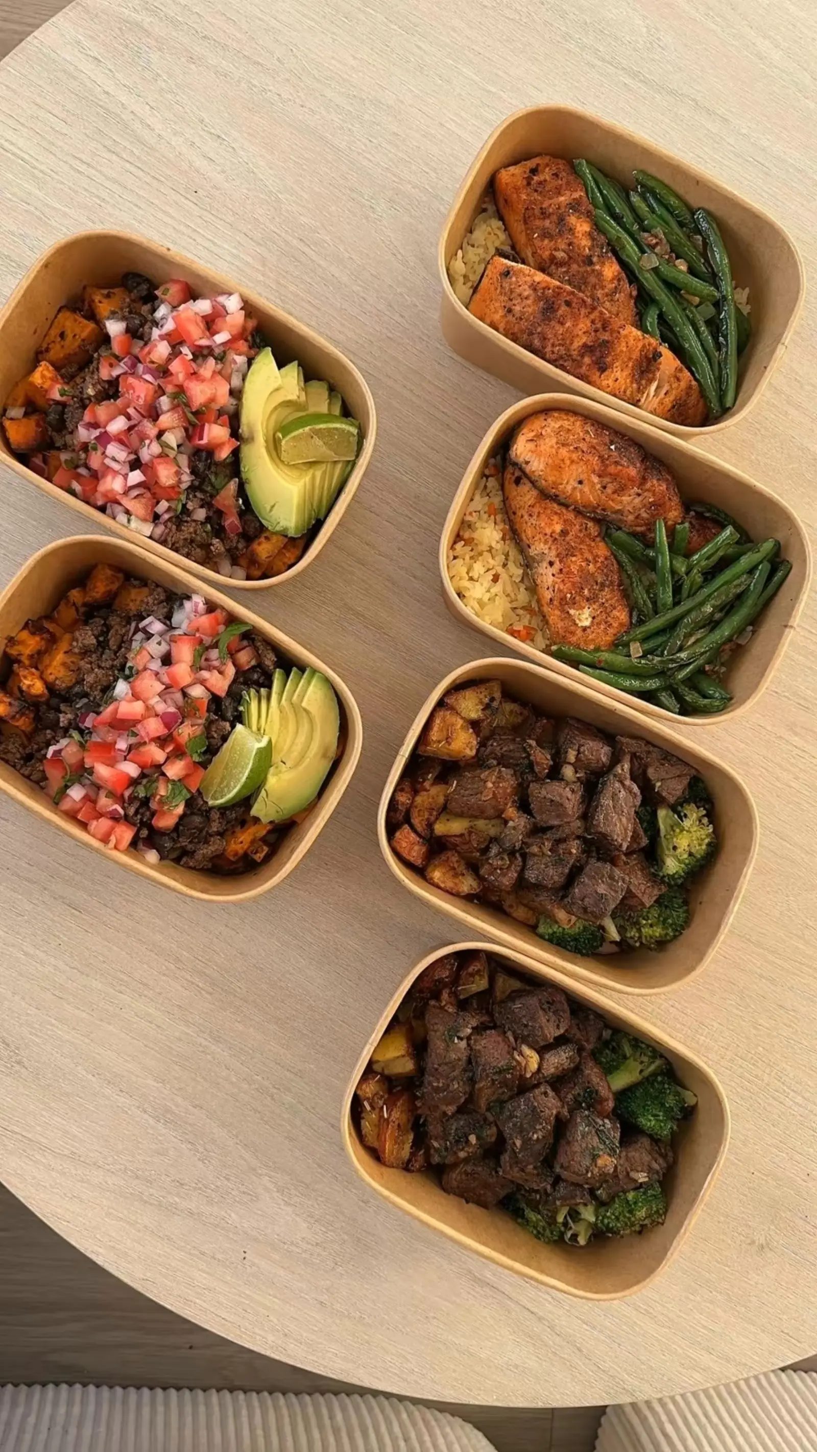 Open meal-prep containers with salmon, chicken, beef, avocado and vegetables